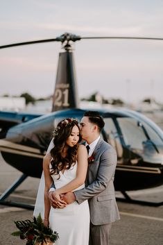 a newly married couple standing in front of a helicopter