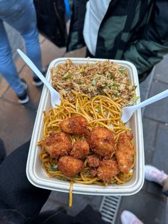 a person holding up a tray of food with noodles and meatballs in it on the street