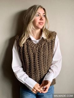 a woman standing next to a wall wearing a brown knitted sweater vest and white shirt