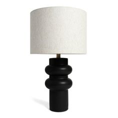 a black table lamp with a white shade on the base and a light in front of it