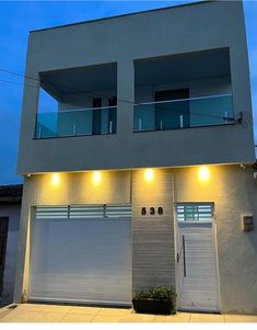 two garage doors are open in front of a house with lights on the windows and balconies