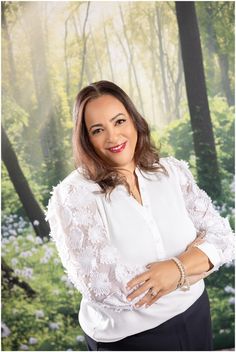 a woman in white shirt and black pants posing for a photo with trees behind her