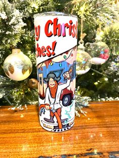 a christmas ornament next to a cup on a table with a tree in the background