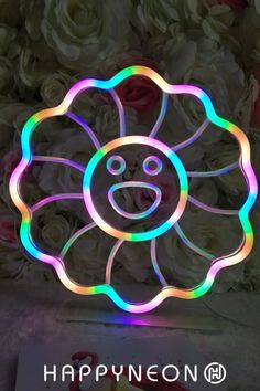 a flower with a smiley face on it and flowers in the background that say happyneon