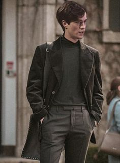 a young man is walking down the street with his hand in his pocket and wearing a black jacket