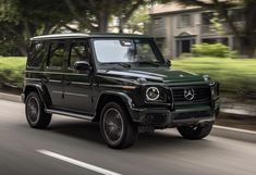 a green mercedes g - class driving down the road