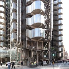 people walking on the sidewalk in front of a tall building with spirally staircases