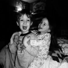 two young children sitting on top of a bed in the dark, laughing at each other