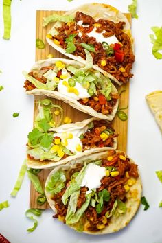 three tacos with meat, lettuce and sour cream on top sitting on a cutting board