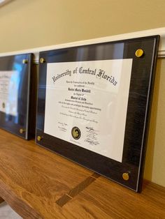 three framed diplomas on a wooden shelf