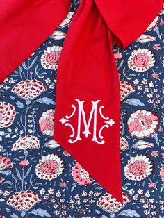 the monogrammed neck tie is on top of a blue and red floral print shirt