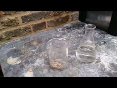 two empty glass beakers sitting on top of a table next to a brick wall