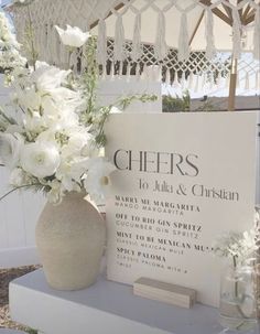 white flowers are in a vase next to a sign with the names of wedding guests