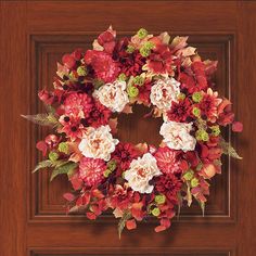 a red and white flower wreath on a wooden door with brown trim around it's edges