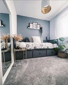 a room with a bed, mirror and plants on the floor in front of it