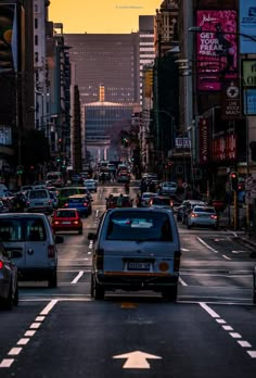 a city street filled with lots of traffic and tall buildings in the background at sunset