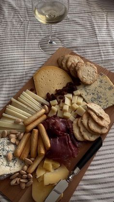 an assortment of cheeses and crackers on a cutting board with a glass of wine