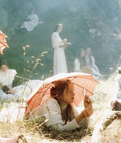 a woman sitting on the ground with an umbrella in her hand and other people behind her