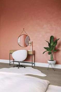 a bedroom with pink walls, white bedding and a round mirror on the wall