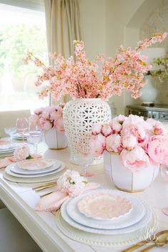 the table is set with pink flowers in vases, plates and napkins on it