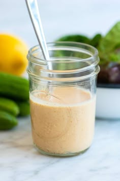 a glass jar filled with dressing next to cucumbers and lemons