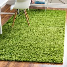 a green rug in the corner of a room with a white chair and computer desk