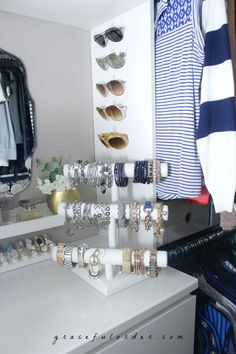 a white dresser topped with lots of bracelets and jewelry next to a wall mounted mirror