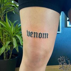 a woman's leg with the word venom tattooed on it and a potted plant in the background