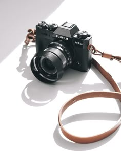 a camera sitting on top of a white table next to a brown leather strap that is attached to it