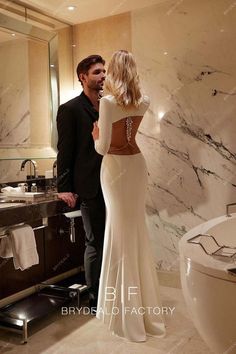 a man standing next to a woman in front of a bathtub and sink with marble walls