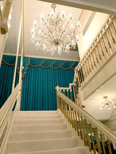 a chandelier hanging from the ceiling next to a set of stairs with blue drapes