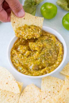 someone dipping salsa into a white bowl with tortilla chips