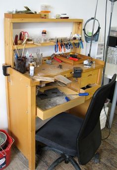 a wooden desk topped with lots of clutter and crafting supplies next to a black chair