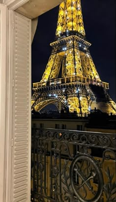 the eiffel tower is lit up in yellow and blue at night, as seen from an open window