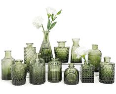 an assortment of green glass vases with white flowers in the middle one is empty