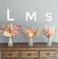 three vases filled with dried flowers sitting on top of a wooden table next to a wall