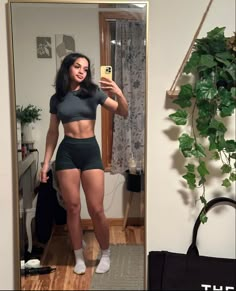 a woman taking a selfie in front of a mirror wearing black shorts and grey top