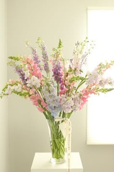 a vase filled with lots of flowers on top of a white table next to a window