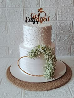 a white wedding cake decorated with baby's breath and the words go engaged on top