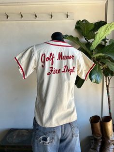 a man standing next to a plant wearing a white shirt with red writing on it