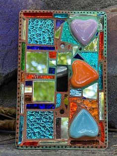 there is a glass tile with different shapes and colors in it on the table next to some rocks