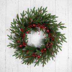 a christmas wreath hanging on the side of a white wooden wall with red berries and pine cones