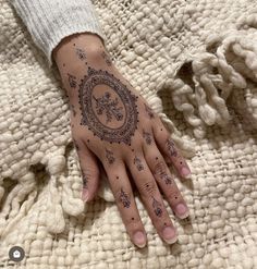 a woman's hand with henna tattoos on it and a white blanket behind her