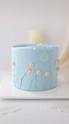 a blue cake with pink flowers on it sitting on top of a white plate next to a candle