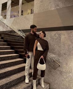 a man and woman standing next to each other in front of some stairs holding bags