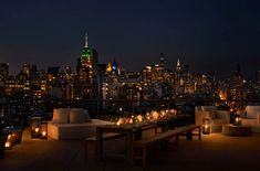 an outdoor dining area overlooking the city at night with lit candles on tables and benches