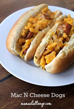 two hotdogs with cheese and bacon on a white plate sitting on a wooden table