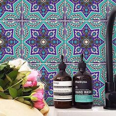 two bottles of hand wash sitting on a counter next to flowers and a vase with roses