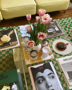 a coffee table topped with magazines and vases filled with pink flowers next to a couch