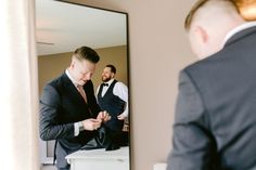 a man in a suit looking at himself in the mirror while another man stands behind him